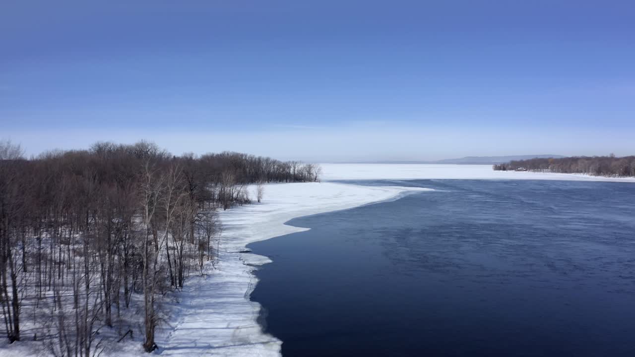 겨울에 숲 근처의 강둑을 따라 날아가는 드론