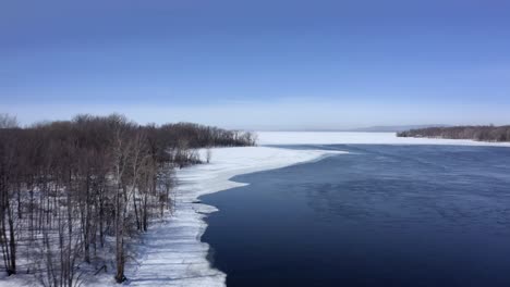 drone flying along a river bank near a forest in winter