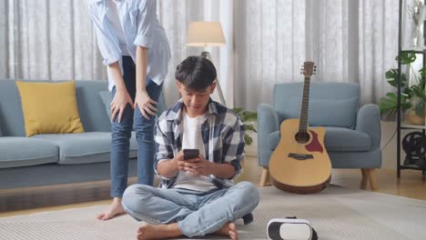 full body asian teen couple, a girl coming home surprising her boyfriend who sits on the floor playing smartphone