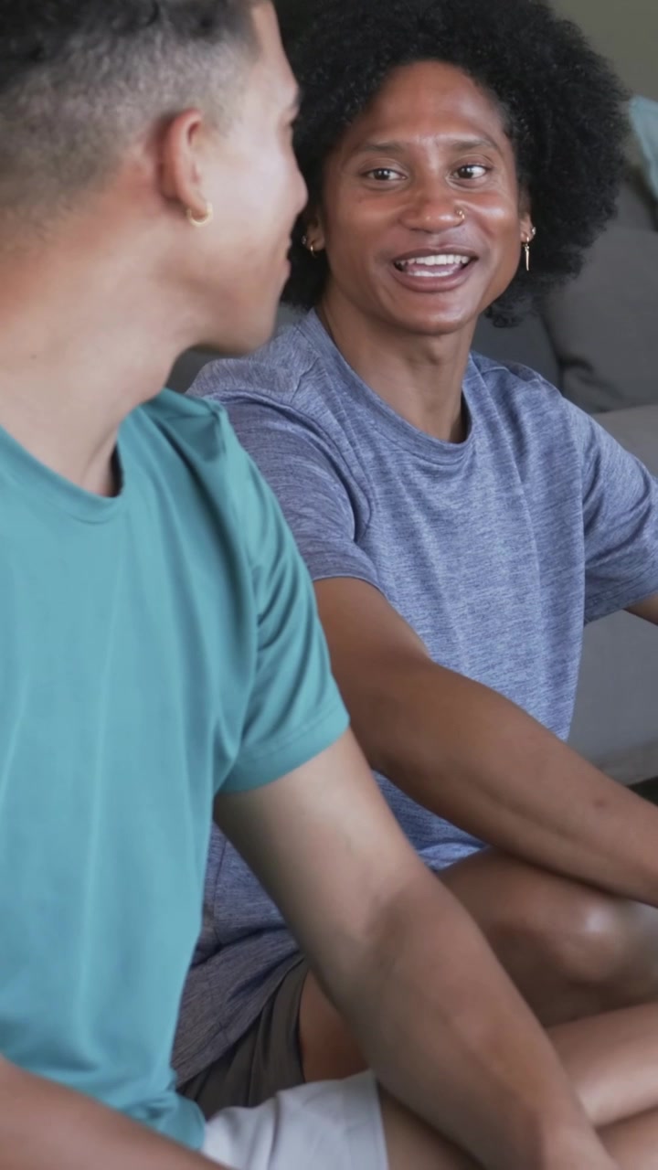 Vertical video: Turning left man in teal shirt initiating chat at lounge sofa, right man smiling
