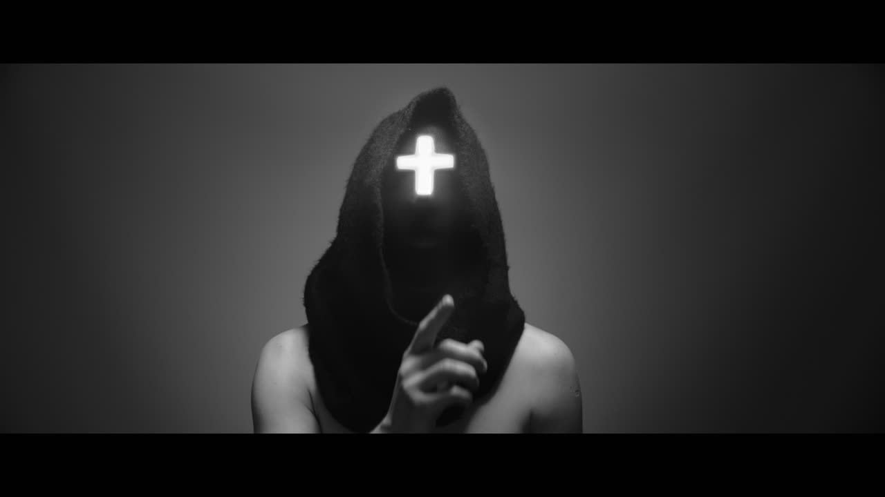 Masked man with cross of light glowing on his face makes a silence gesture