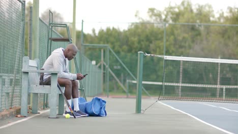 Happy-african-american-man-using-smartphone-sitting-on-bench-at-tennis-court,-slow-motion