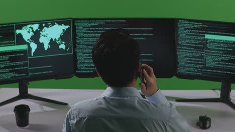 그린 스크린 스튜디오에서 여러 컴퓨터 화면으로 코드를 작성하는 동안 휴대 전화로 대화하는 아시아 남자 개발자의 뒷면