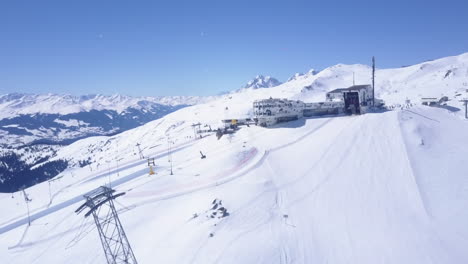 Hacia-Delante-Vuela-Por-Encima-De-La-Empinada-Pista-De-Esquí-En-Las-Montañas-De-Invierno.-En-Dirección-A-La-Estación-Superior-Del-Teleférico-Con-Restaurante-Y-Hotel-En-Crap-Sogn-Gion.-Laax,-Suiza