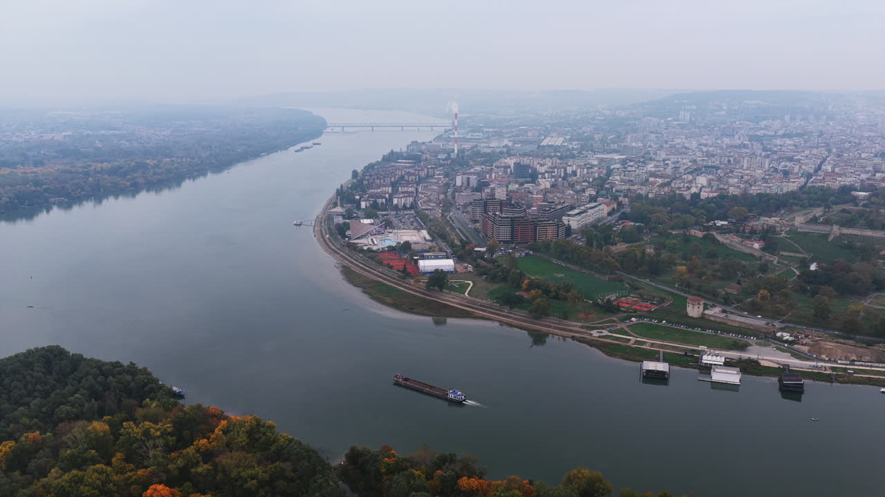 An aerial look along Belgrade’s riverbank with residential blocks, promenades, rail lines, and flowing water stretching toward distant bridges