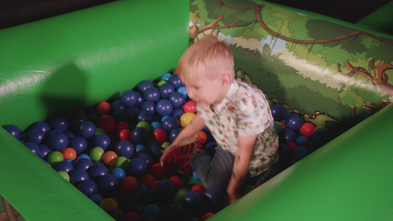 niño jugando en la piscina de bolas, sonriendo y lanzando las bolas