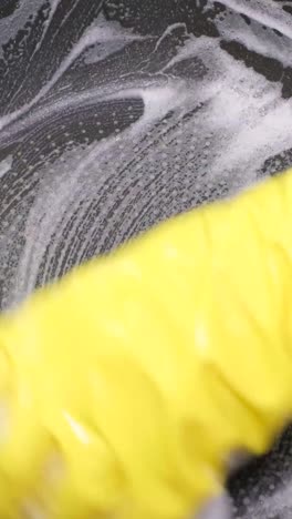 hand in yellow glove scrubbing a surface with soap suds