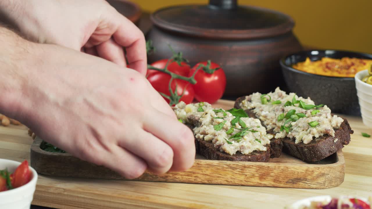 cocina israelí. manos poniendo forshmak con pan de centeno negro decorado con perejil en primer plano. plato nacional de arenque judío, cultura de oriente medio. bocadillo tradicional vorschmack hecho de filete de pescado