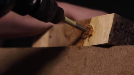 carpenter using an electric drill to make a hole in a thick slab of a treetrunk that has been smoothed down