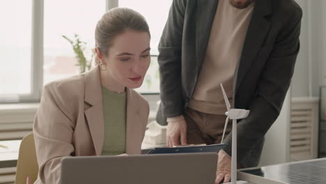 close up view of woman using laptop sitting at table next to windmill model in the office