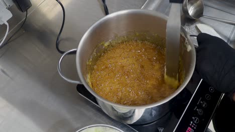 chef cocinando postre con mantequilla salada, caramelo, hervido, estirado con espátula, salsa salada caliente y suave cocida en una sartén de acero en la estufa