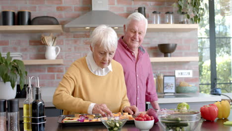 happy senior caucasian couple cooking dinner in kitchen at home, slow motion