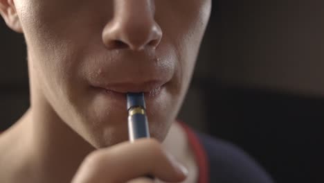 man putting the mouthpiece tip of a vape pen on his mouth - closeup shot