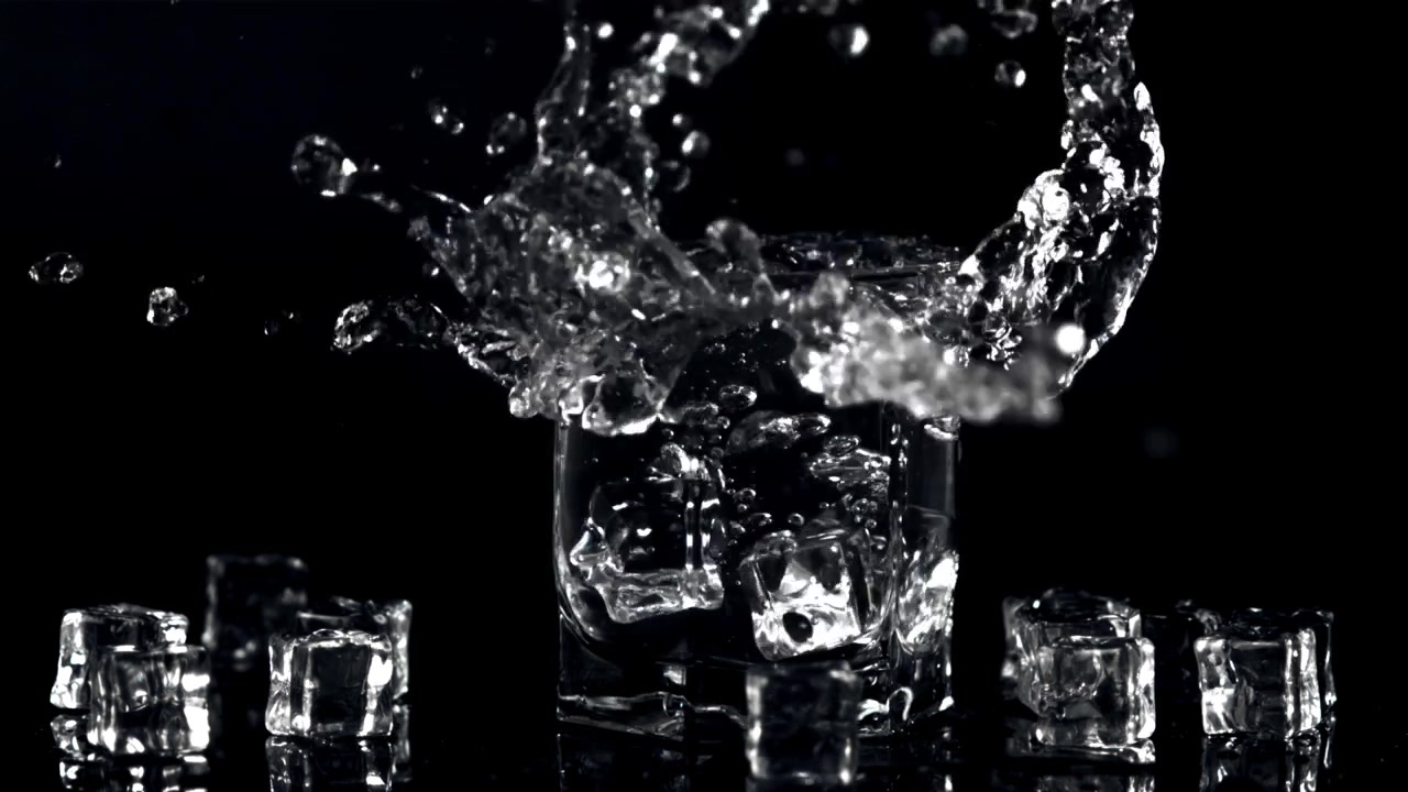 Vertraagde beweging van ijsblokjes die in een glas water spatten.