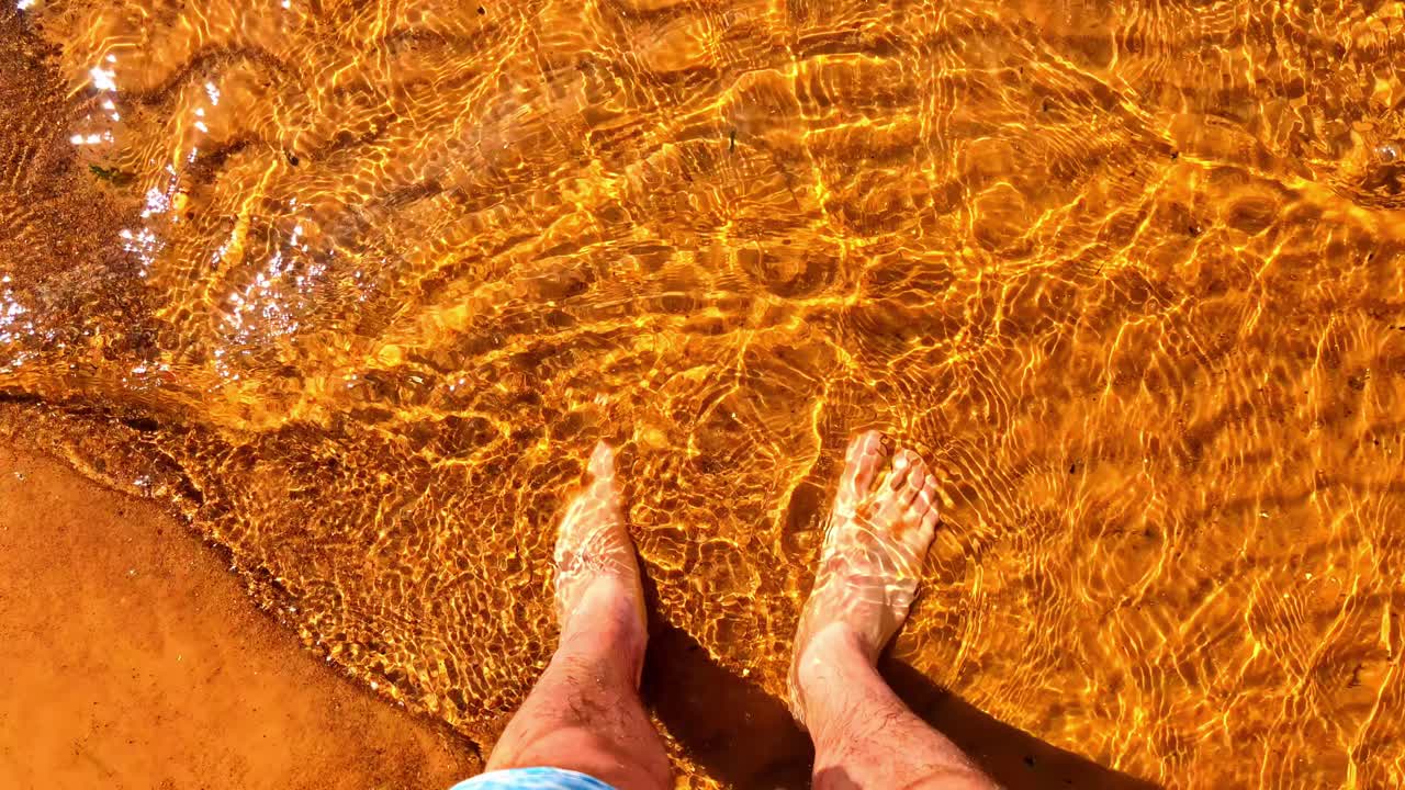 Bare Feet Standing in Clear and Shallow Golden Sea Shore Water With Sun Reflections