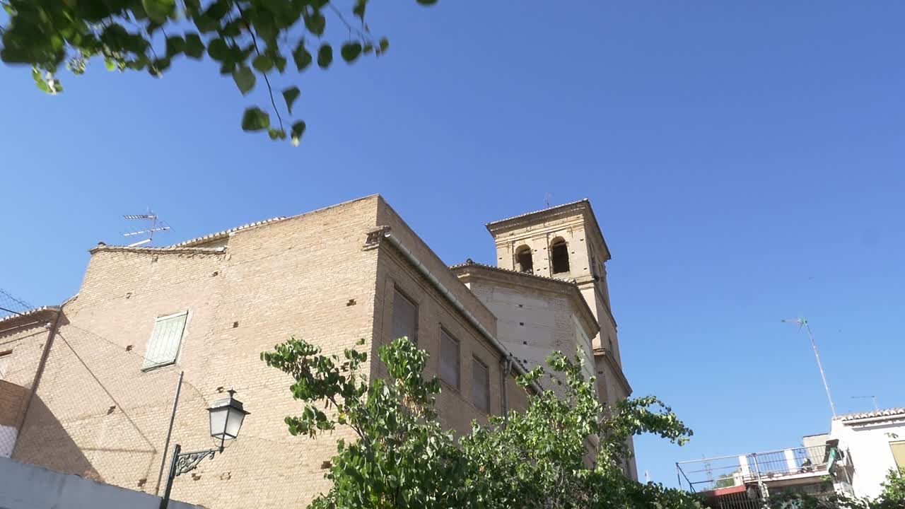 Inquadratura dal basso verso l'alto che rivela il campanile della Chiesa di El Salvador a Granada. Incorniciato da lussureggianti foglie verdi contro un cielo azzurro e limpido. Architettura religiosa tradizionale spagnola