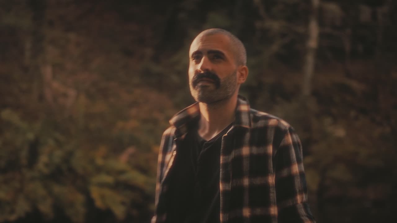 Man by river in forest enjoys golden sunlight and nature. He feels calm and peaceful. Soothing and warm nature clip