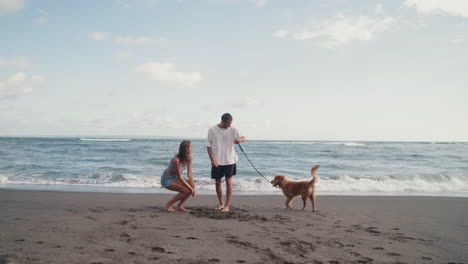 una pareja jugando con un perro cerca del océano.