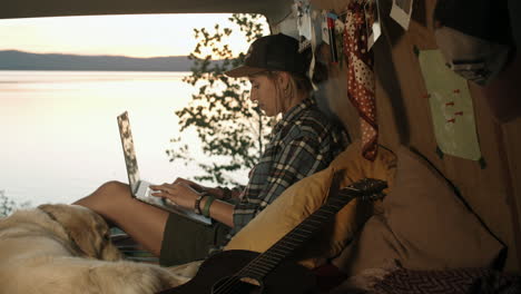 Mujer-Usando-Una-Laptop-En-Una-Camioneta-Al-Atardecer-En-La-Orilla-Del-Lago