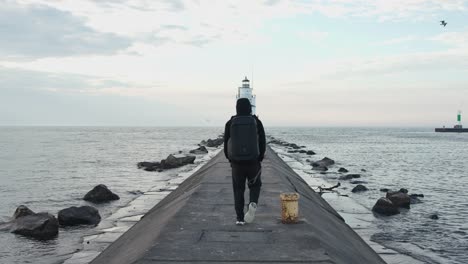 man with hoodie walking towards the lighthouse with book bog