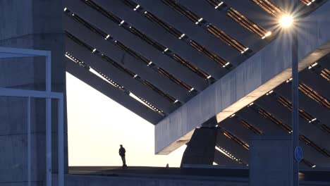 young male riding electric scooter under massive geometric solar structure in urban city street