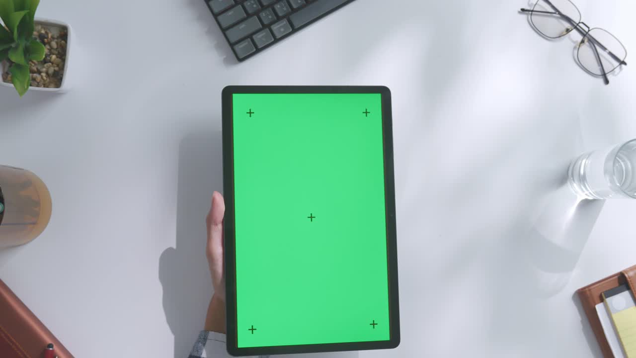 초록색 화면을 모방한 노트북 컴퓨터의 상단에서 아래로 볼 때, 펜, 안경, 그리고 물 한 잔을 가진 노트북 에 나무 사무실 책상 위에 크로마키 디스플레이가 있습니다.