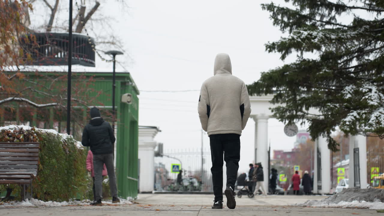색 겨울 재을 입은 소년이 바쁜 도시 환경을 특징으로하는 흐릿한 배경으로 도시 길을 고있는 뒤쪽 모습, 도시 생활 가운데 평화로운 겨울 산책을 설명합니다.