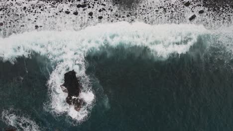 Aerial-view-of-waves-crushing-into-a-pebble-beach,-turquoise-water-and-white-foam