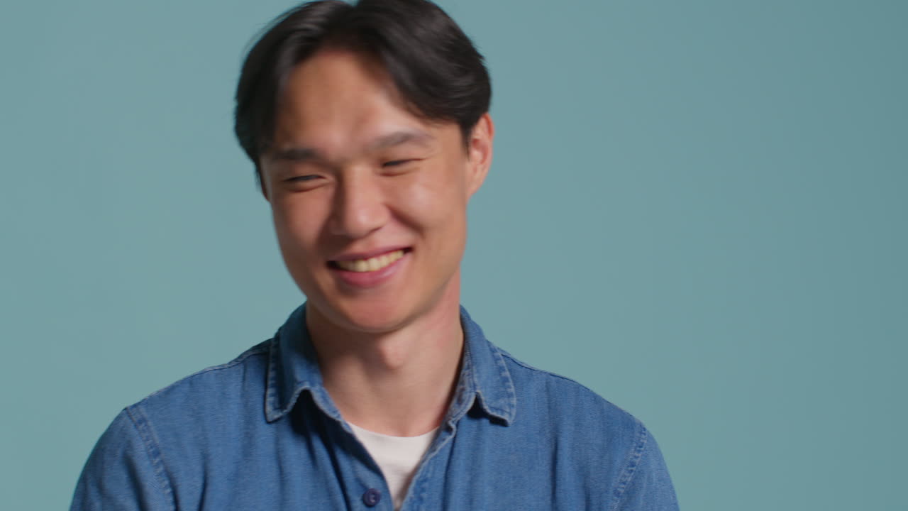 파란 스튜디오 배경 앞의 남자가 사진 부스 스타일의 초상화를 위해 재미있게 포즈를 취하고 얼굴을 끌고 있습니다.