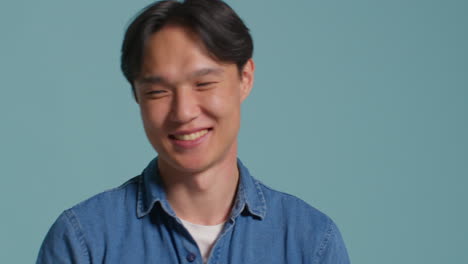 파란 스튜디오 배경 앞의 남자가 사진 부스 스타일의 초상화를 위해 재미있게 포즈를 취하고 얼굴을 끌고 있습니다.
