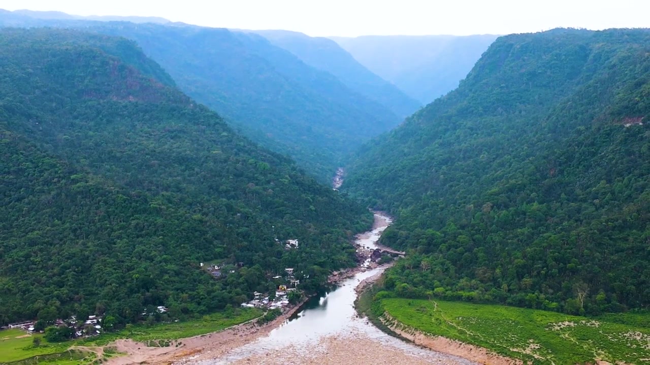 Dòng sông khô cạn trên đồi, thung lũng sông uốn lượn được bao quanh bởi những ngọn đồi Meghalaya dốc, phủ rừng gần khu vực biên giới Bangladesh-Ấn Độ tại Bichanakandi, ảnh drone góc rộng từ trên cao, ban ngày, ánh sáng u ám.