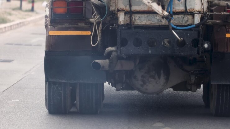 A truck emits smoke while driving on a road in Phuket, Thailand, highlighting pollution issues. The scene captures urban traffic dynamics