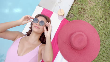 a woman in a pink swimsuit relaxes by the pool, adjusting her sunglasses