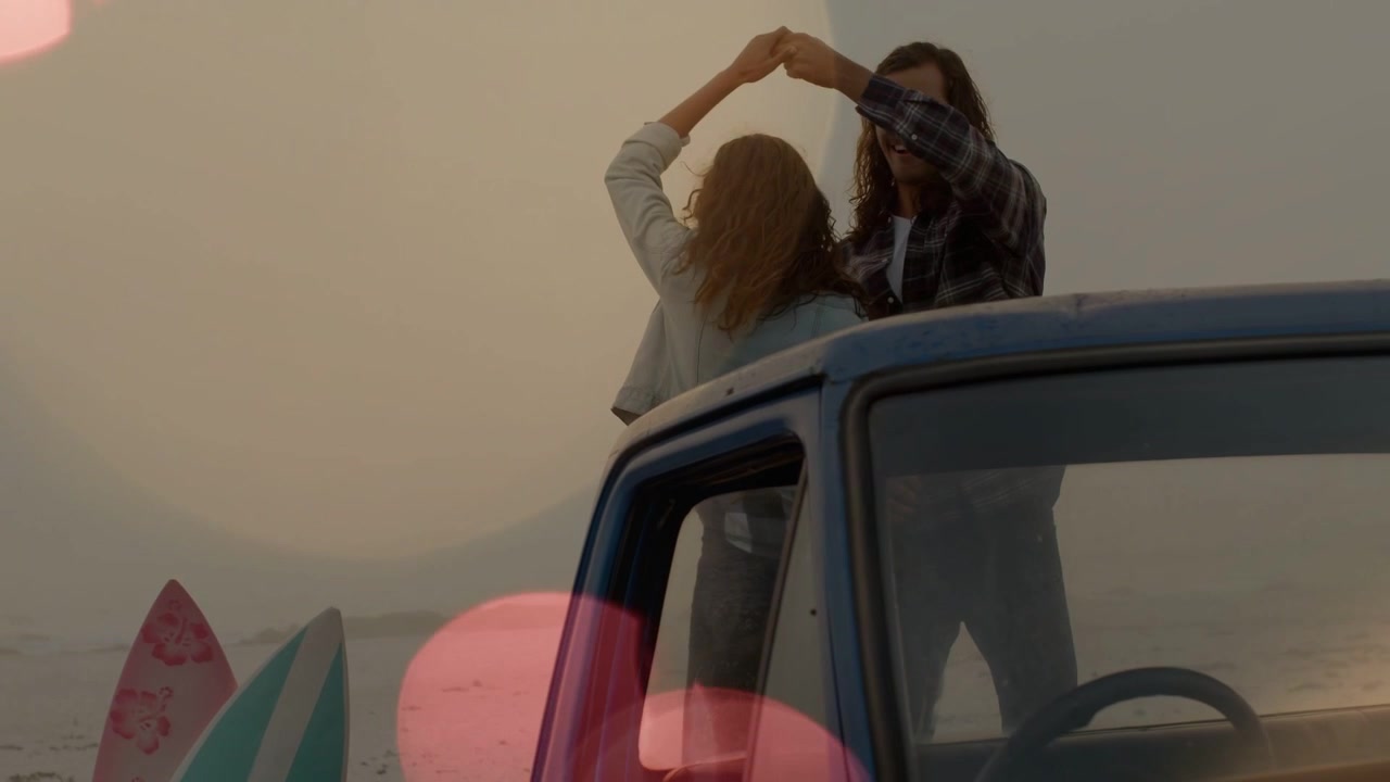 Una coppia che si abbraccia mentre sale su un pickup blu, formando un cuore sopra le tavole da surf, per il marketing turistico.