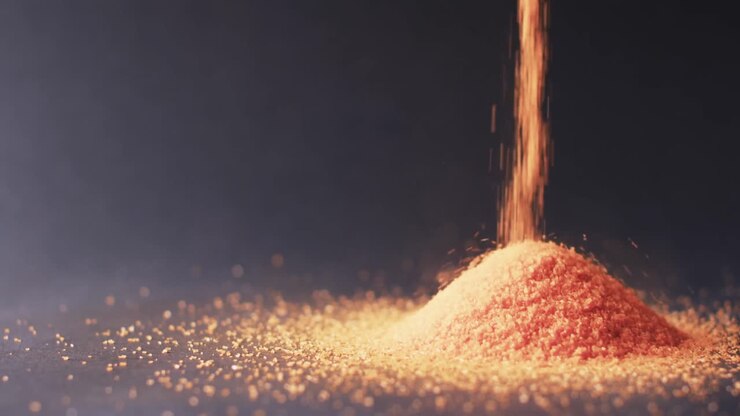 Video ravvicinato di granelli di sabbia arancioni che cadono a formare un cumulo e spazio per il testo su sfondo nero.