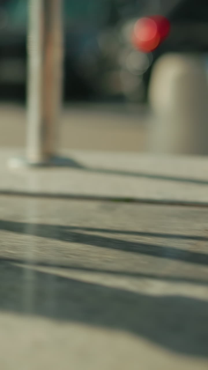 Side view of lady in heels walking by iron railing casting long shadow on ground with blurred parked and moving cars in background under bright sunlight