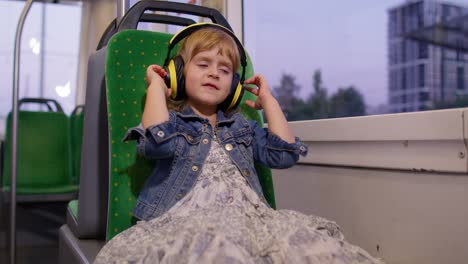 Lovely-child-girl-wearing-headphones-listening-music,-relax-dancing-while-traveling-by-bus-in-city