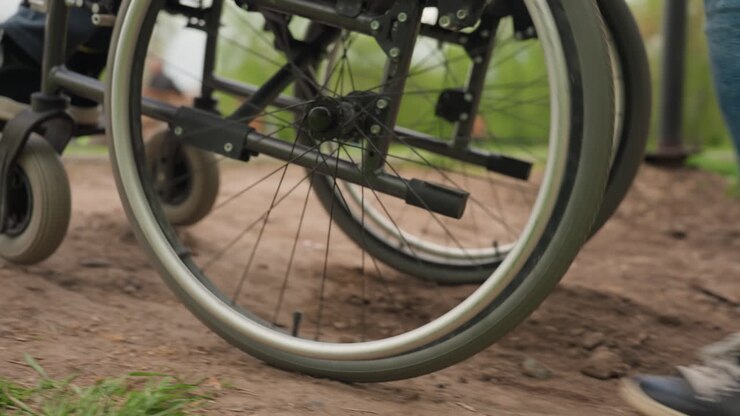 Sedia a rotelle su terreno accidentato, immagine dettagliata delle ruote di una sedia a rotelle che superano ostacoli esterni, vista focalizzata sulle ruote di una sedia a rotelle che manovrano su terreni esterni impegnativi con assistenza