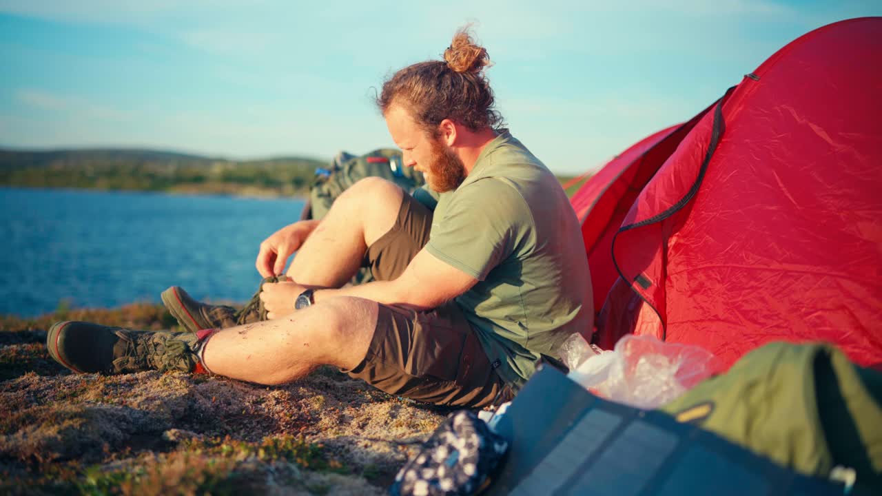 텐트 캠핑 근처 에서 부츠 를 벗고 있는 백인 산책자