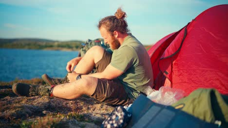 excursionista caucásico quitándose las botas cerca del campamento de tiendas de campaña