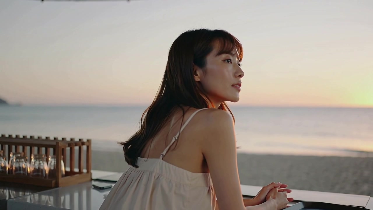 Coming from right woman in sundress holding dark tray leaning on beach bar counter seeking sunset