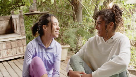 sitting on porch, two multiracial female friends having friendly conversation and smiling together