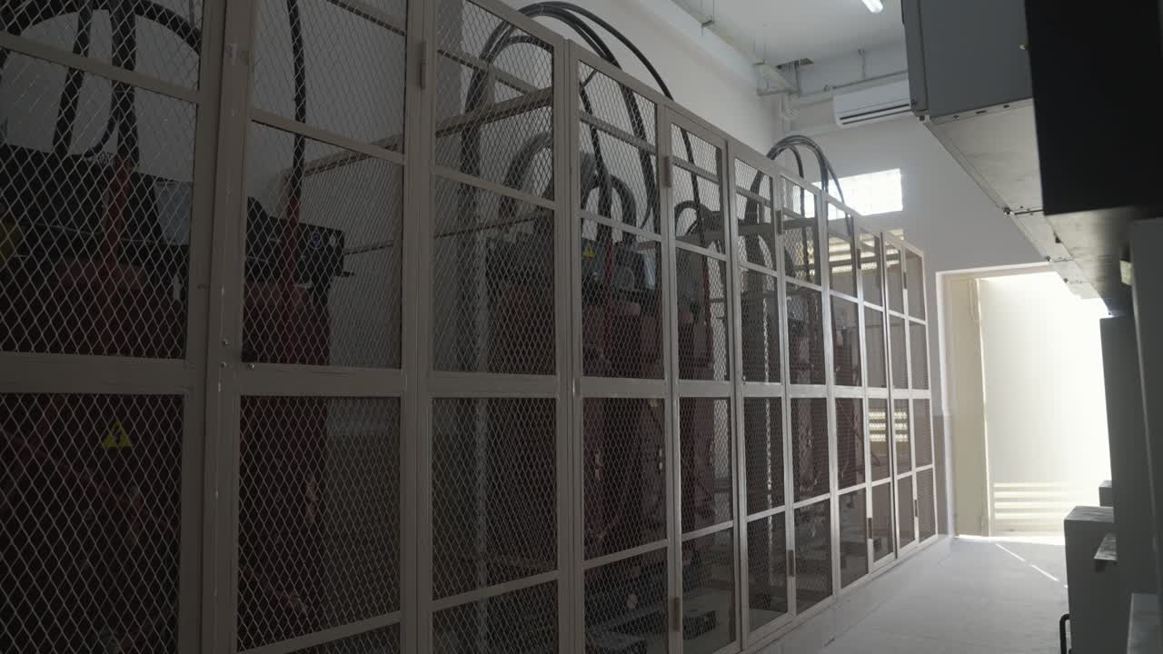An interior shot of an industrial power room. Large, high-voltage electrical cabinets, transformers, or servers are secured behind protective metal mesh cages