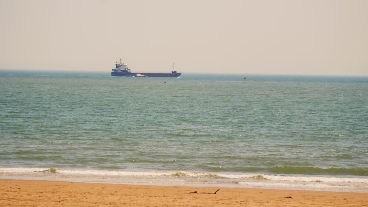 Container Ship Travelling Along Bay After Unloading Cargo at Nearby Port with Support Vessel with Sandy Beach. Headed to Destination to Pick Up Goods for Importing and Exporting Shipping.