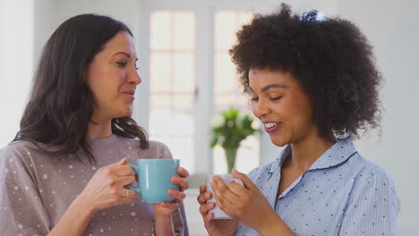loving same sex female couple wearing pyjamas drinking morning coffee in kitchen at home