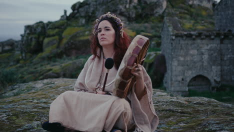 spiritual-woman-playing-a-shamanic-drum-in-a-beautiful-medieval-village-track-in-shot