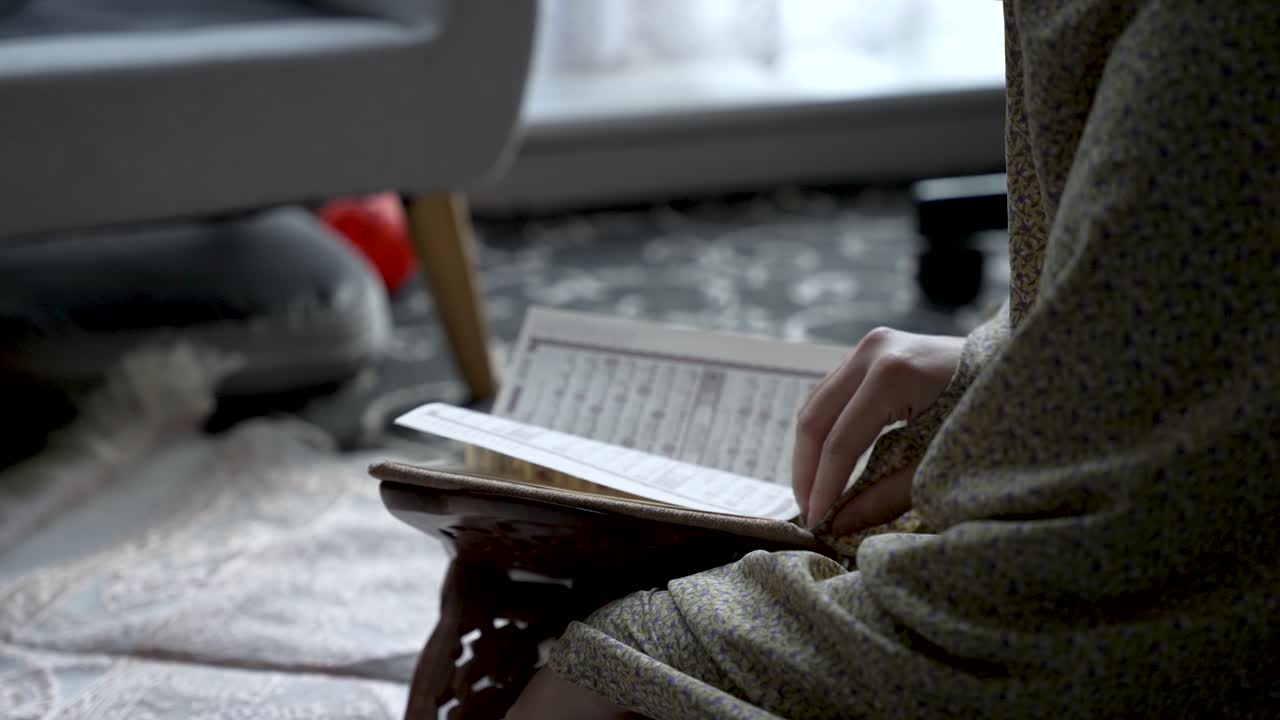 Persona che legge il Corano in una stanza in penombra, con focus sul testo e sulle mani, in un'atmosfera accogliente.
