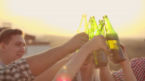 young people clinks glasses and drinks cold beer from colorful green bottels on the party with friends on the roof.