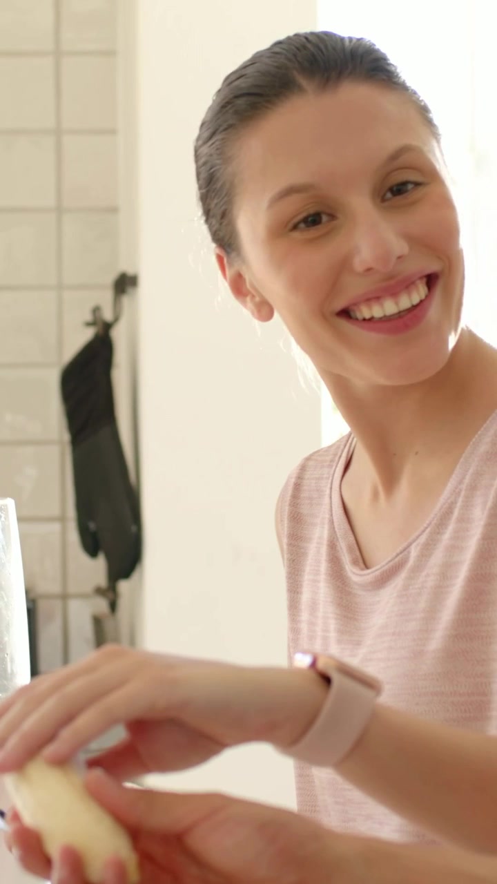 Video verticale: Telecamera che si allontana, donna con un top rosa che sbuccia una banana in un frullatore da cucina