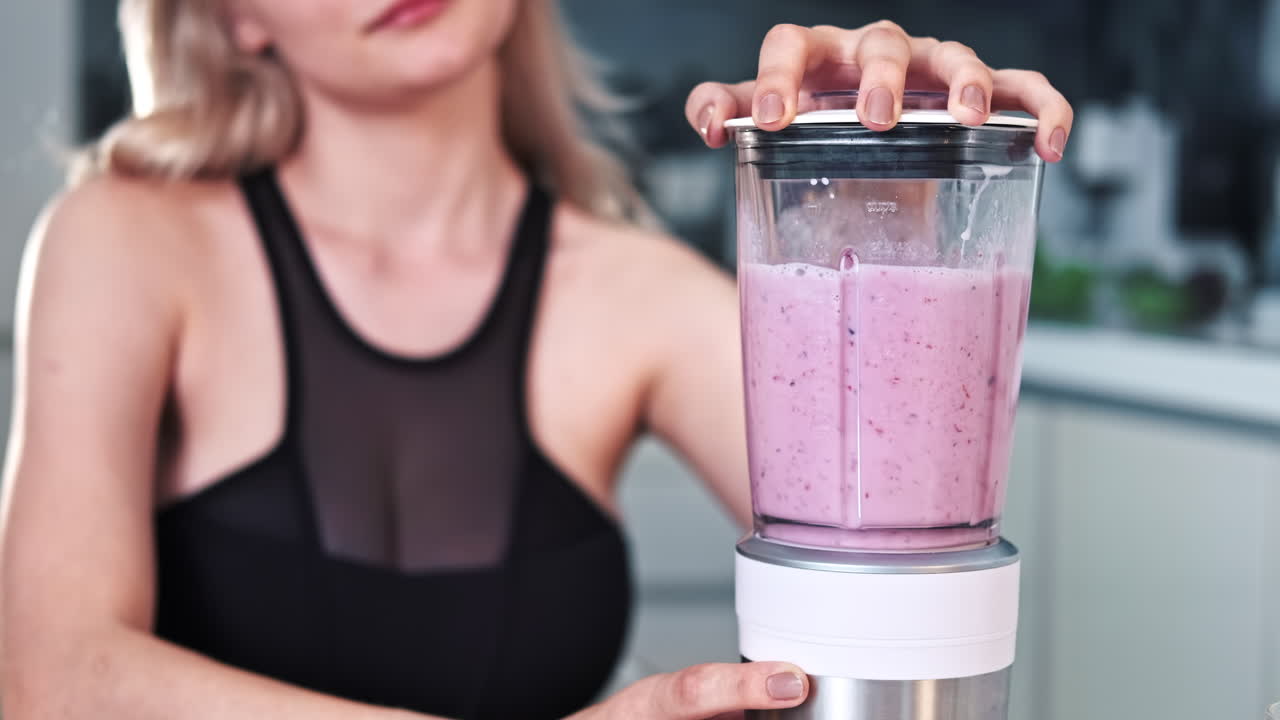 A young blonde woman making a milkshake of fruits and berries. Blueberry, strawberry, banana. Healthy food idea
